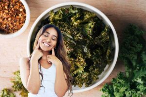 in primo piano una donna che simula con le mani qualcosa di buono e per sfondo una ciotola di chips di cavolo nero