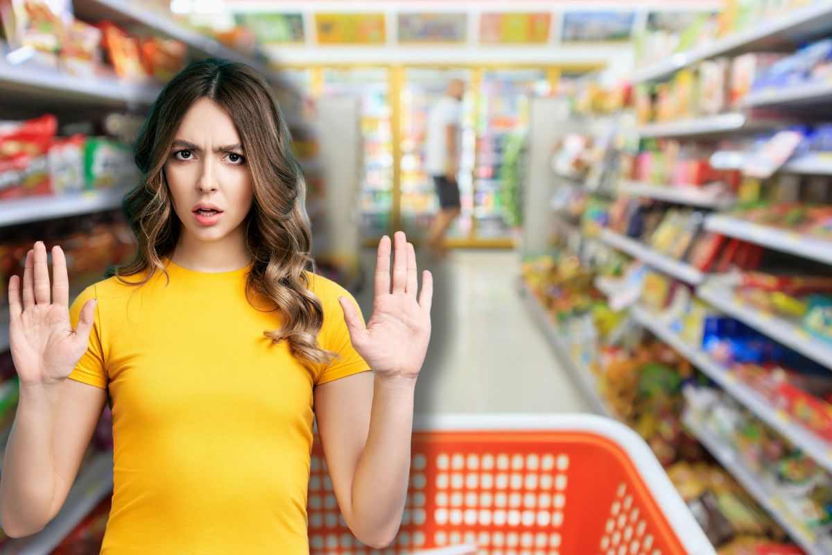 carrello tra le corsie di un supermercato e donna che fa stop con le mani